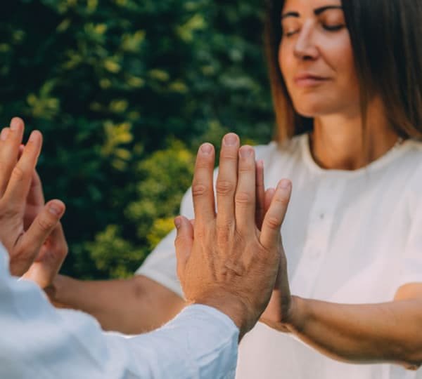 A woman engaging in energy healing therapy, practicing mindfulness with a partner outdoors.