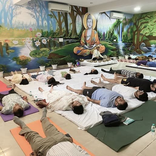 A group of individuals lying in a guided relaxation session at a wellness center, surrounded by a peaceful Buddha-themed mural, promoting stress relief and holistic healing.