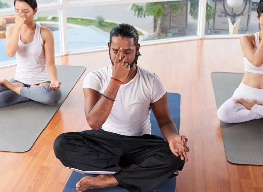 A yoga instructor leading a group in pranayama breathing exercises courses, promoting mental clarity and well-being at a wellness retreat.