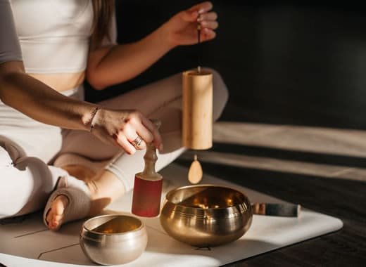 A woman practicing sound healing therapy in mind therapy courses with Tibetan singing bowls and chimes, promoting relaxation and inner balance at a wellness center.